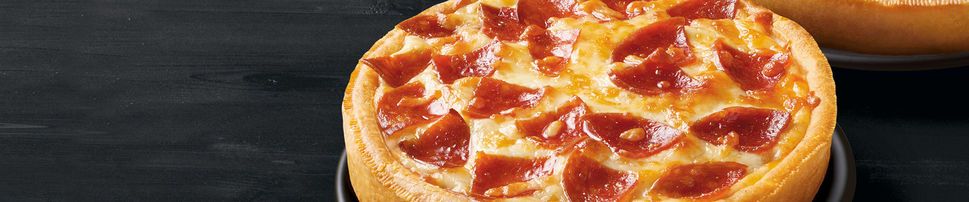 A cooked RED BARON® Singles Pepperoni Deep Dish Pizza on a black dish